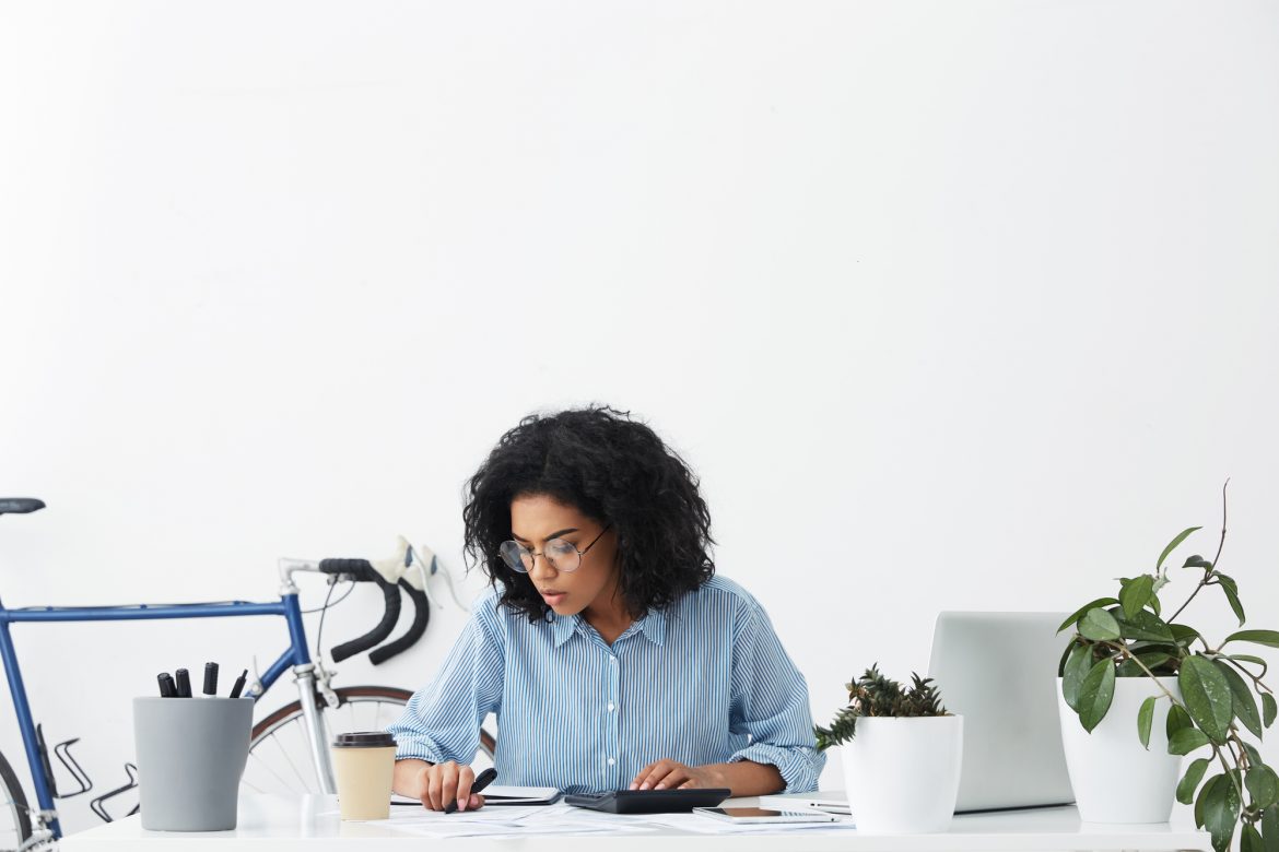 Attractive mixed race housewife looking concentrated while calculating bills at home, planning domestic budget, making notes and analyzing receipts all over table. People and finances concept autonomos
